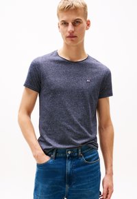 T-shirt bleu marine à manches courtes avec un motif texturé, col rond et petit logo sur la poitrine, associé à un jean en denim bleu.