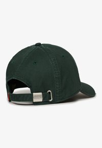 Gorra de béisbol de algodón verde oscuro con visera curvada, correa ajustable y herrajes metálicos que exhiben el nombre de la marca. Tela texturizada visible.