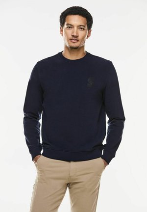 Sudadera de cuello redondo azul marino hecha de tela de algodón, con un logo sutil en el lado izquierdo del pecho y puños y dobladillo acanalados.