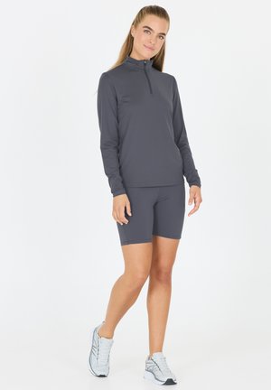 Athletic outfit featuring a fitted, long-sleeve, dark gray top with a zip collar and matching short gray shorts. Worn with light gray shoes.