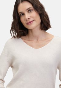 Helles beiges, geripptes Sweatshirt mit V-Ausschnitt, langen Ärmeln und weicher Textur. Entworfen für einen bequemen Sitz.