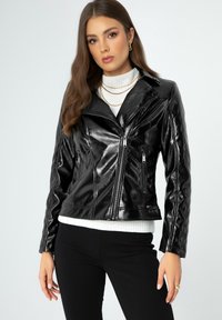 Schwarze Kunstleder-Bikerjacke mit glänzender Oberfläche, gesteppte Details an den Ärmeln, Reißverschluss-Taschen und tailliertem Design.