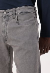 Grå denim jeans med slim fit, som har kontrasterende søm, frontlommer og en sølvfarge knappelukking i midjen.