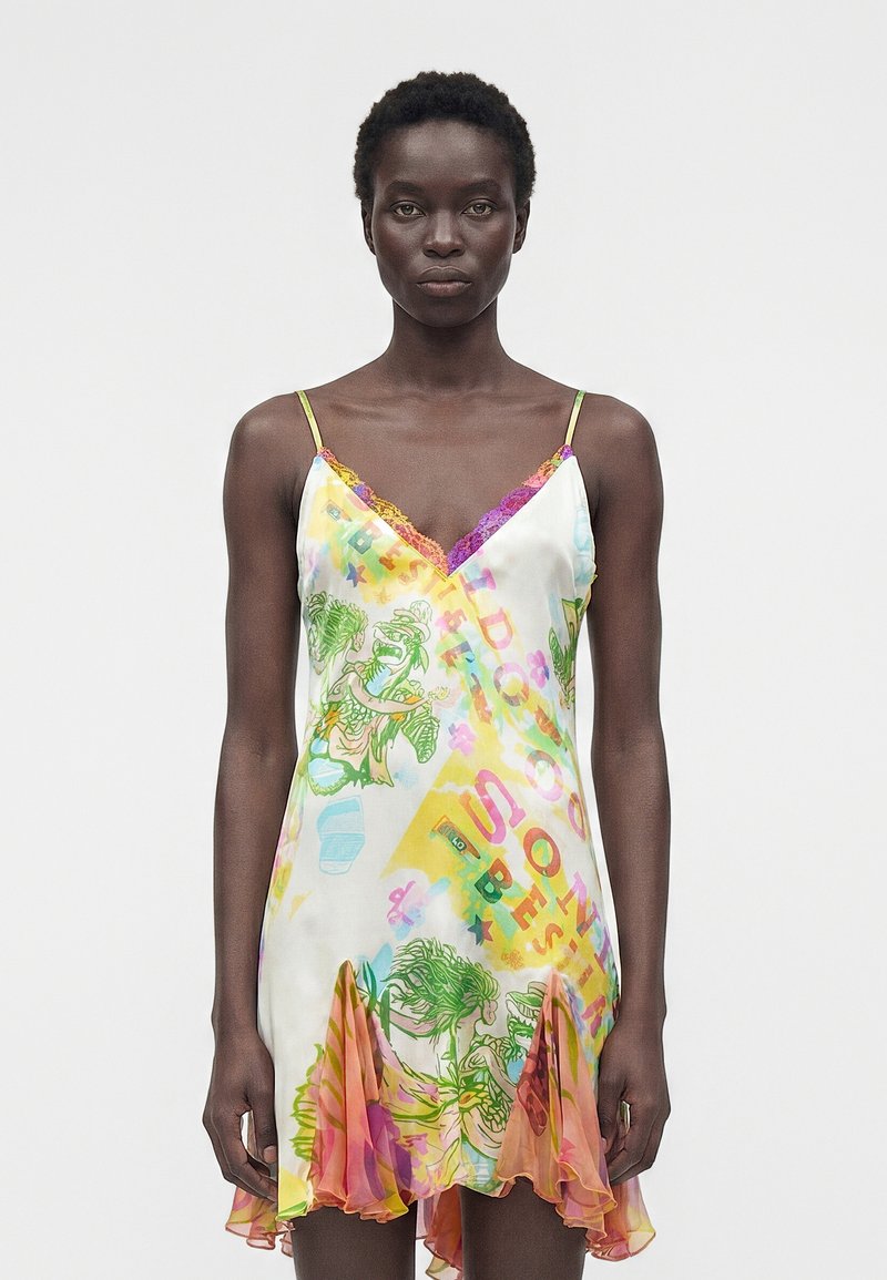 Γυναίκα που φοράει πολύχρωμο φόρεμα-νεγκλιζέ χωρίς μανίκια με γραφικά σχέδια, δαντελένια διακόσμηση και βολάν στο τελείωμα, στέκεται μπροστά σε απλό λευκό φόντο.