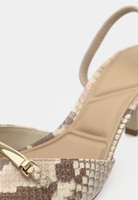 Chaussure à talon haut beige à bride arrière avec un motif texturé en cuir de serpent, dotée d'une boucle dorée et d'une semelle intérieure rembourrée pour plus de confort.