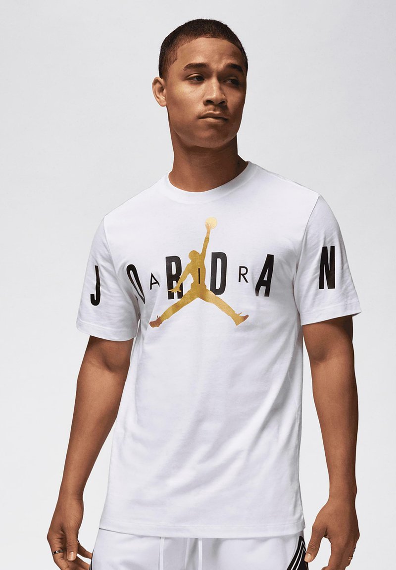 Balts kokvilnas T-krekls ar zelta Jordan logotypu un melnu tekstu "JORDAN" priekšpusē. Īsas piedurknes, standarta piegriezums.