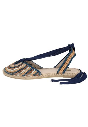 Sandalia plana tipo esparto con parte superior tejida multicolor y cordones azul marino en el tobillo sobre suela beige, vista lateral.