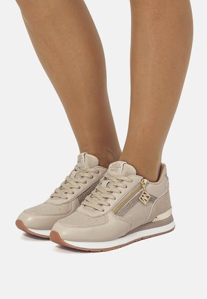 Zapatillas deportivas de cuero beige con detalles texturizados, acabados brillantes y cremallera lateral. Suela clara con base de goma marrón. Los cordones son metálicos.