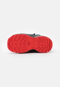 Suela de zapatilla deportiva negra con un destacado patrón de tracción de goma roja que presenta triángulos elevados y protuberancias circulares para mejorar el agarre.