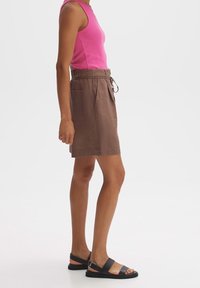 Shorts en lin marron clair avec une taille à cordon et deux poches latérales, associés à un top sans manches rose ajusté et des sandales noires.