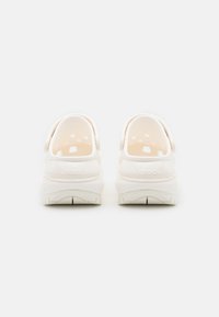 White Crocs with a smooth, glossy finish, round openings on the sides, and a textured rubber outsole, featuring a subtle logo on the heel.