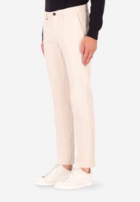 Pantaloni beige realizzati in tessuto misto cotone, design a gamba dritta con tasche laterali e chiusura frontale con bottoni, abbinati a sneakers bianche.