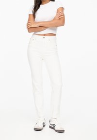 Pantalones de mezclilla blanca con corte ajustado y cintura alta, con cierre frontal de botón y cremallera, bolsillos traseros y detalles de costura mínimos.