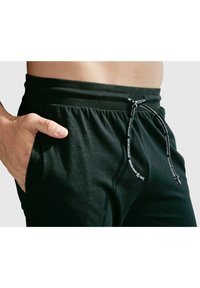 Schwarze Jogginghose aus leichtem Material, mit elastischem Bund und Kordelzug sowie seitlichen Taschen. Glatte Textur.