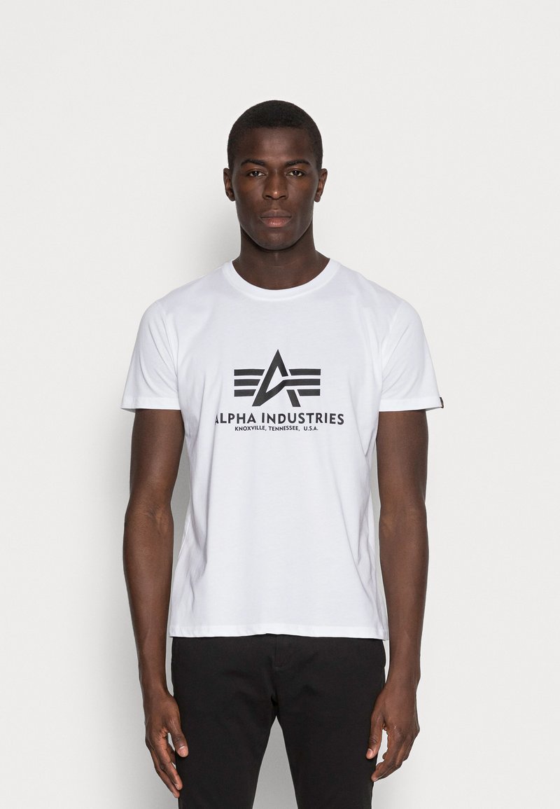 Weißes Baumwoll-T-Shirt mit einem schwarzen "Alpha Industries"-Logo und Grafikdesign. Kurze Ärmel und Rundhalsausschnitt.