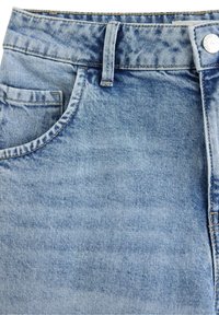 Primo piano di jeans in denim azzurro chiaro che mostra la tasca frontale, il passante per cintura, la vita e la chiusura con bottone metallico con dettagli di cuciture visibili.