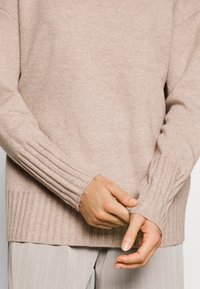 Jasnobeżowy, dziany sweter z prążkowanymi mankietami i dołem. Miękka faktura, lekko oversize'owy krój oraz luźny dekolt. Subtelne detale w designie.