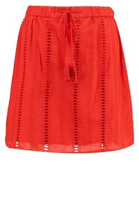 Jupe rouge, arrivant au genou, en tissu léger avec une taille à cordon. Présente des motifs découpés verticaux et des franges à la taille.