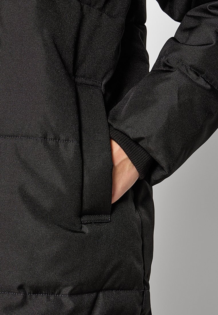 Schwarze gepolsterte Jacke mit einer Seitentasche, glatter Textur und elastischen Bündchen für einen engen Sitz. Der Stoff wirkt strapazierfähig und wetterbeständig.