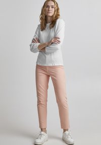 Weißes strukturiertes Langarmoberteil mit rundem Ausschnitt, kombiniert mit rosa verkürzten Hosen. Das Model trägt weiße Sneakers. Einfaches, modernes Design.