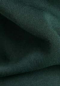Tejido verde oscuro con un punto suave y texturizado. El material parece liso, con costuras finas y uniformes, y una calidad ligeramente elástica.