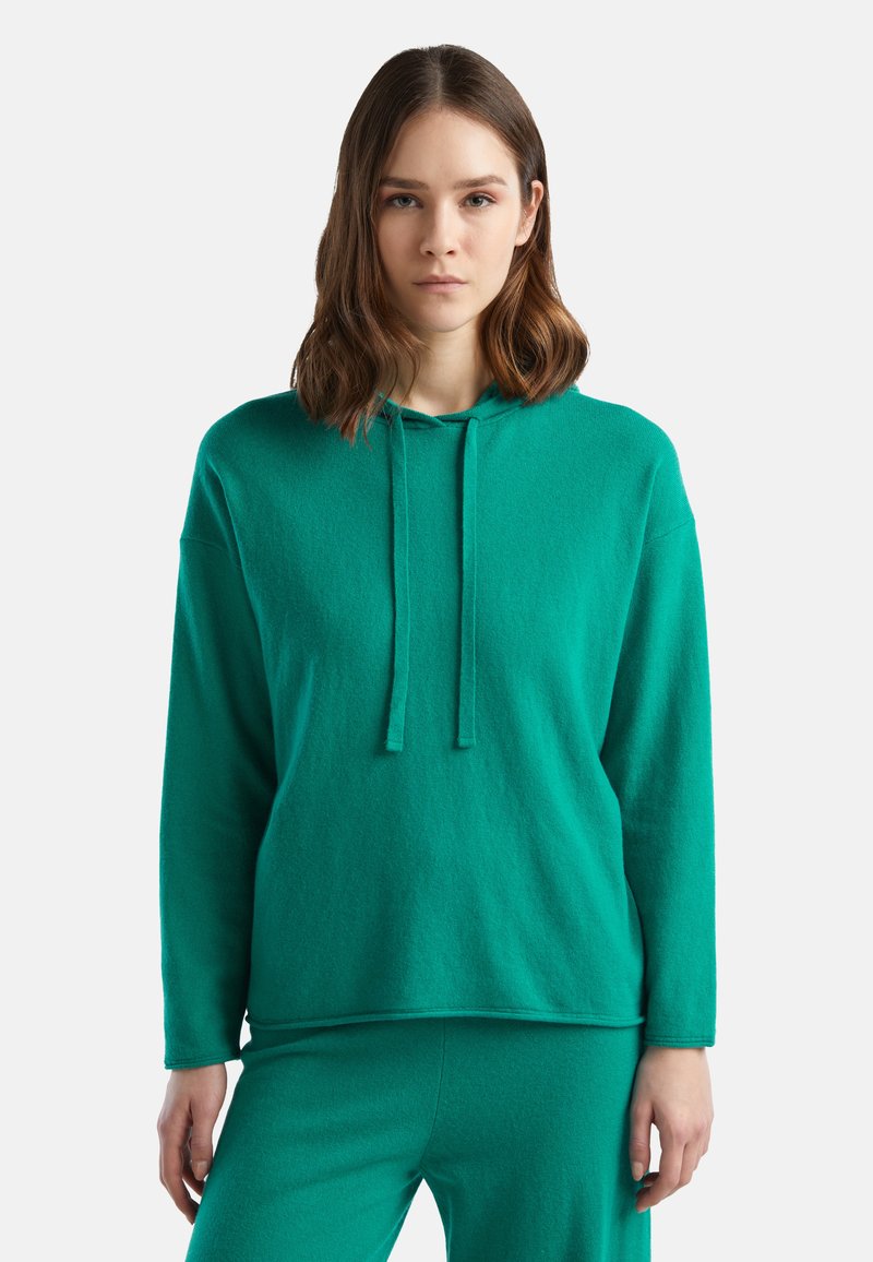 Sudadera con capucha en color verde azulado, hecha de una tela suave, con mangas largas, cordones y un corte relajado, combinada con pantalones a juego.