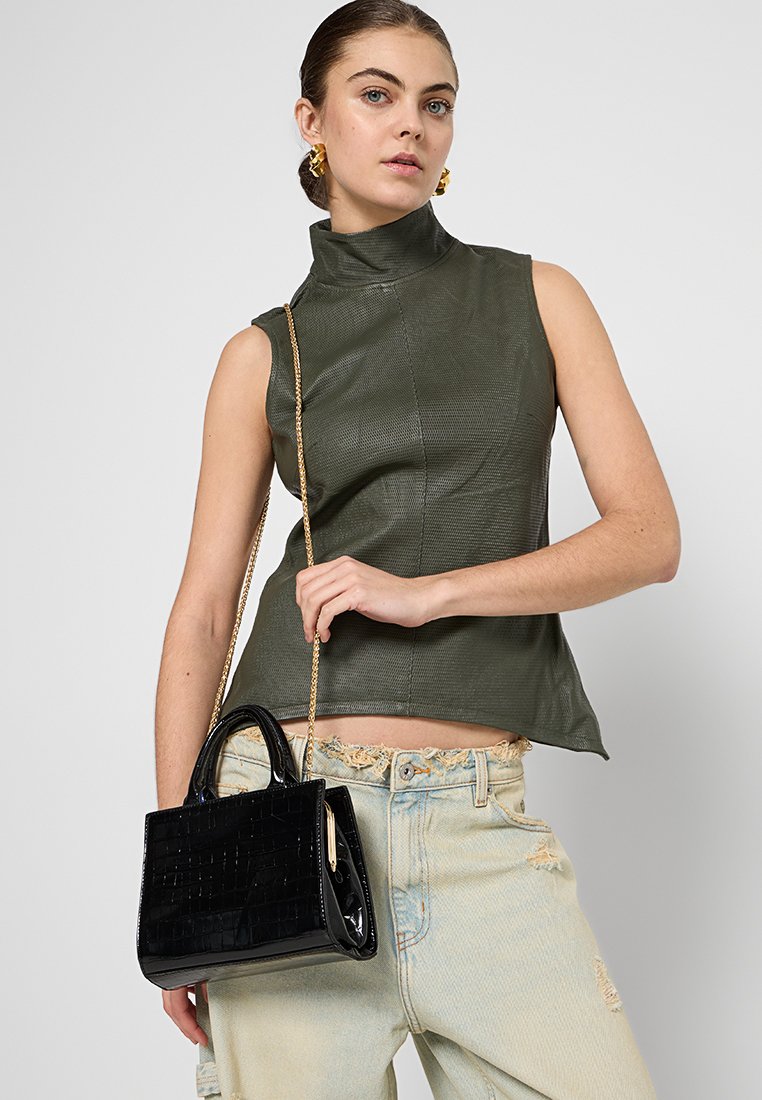 Haut sans manches olive avec un col montant, fabriqué à partir d'un matériau texturé. Accompagné d'un petit sac à main en cuir synthétique noir avec un motif crocodile.