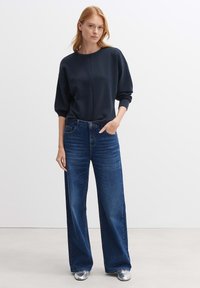 Felpa blu navy con maniche ampie e scollatura rotonda, abbinata a jeans blu a vita alta e gamba larga, e scarpe metalliche argentate.