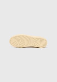 Rubber sneaker sole with a textured design, featuring a wavy pattern in light beige. Notable branding detail on the side.