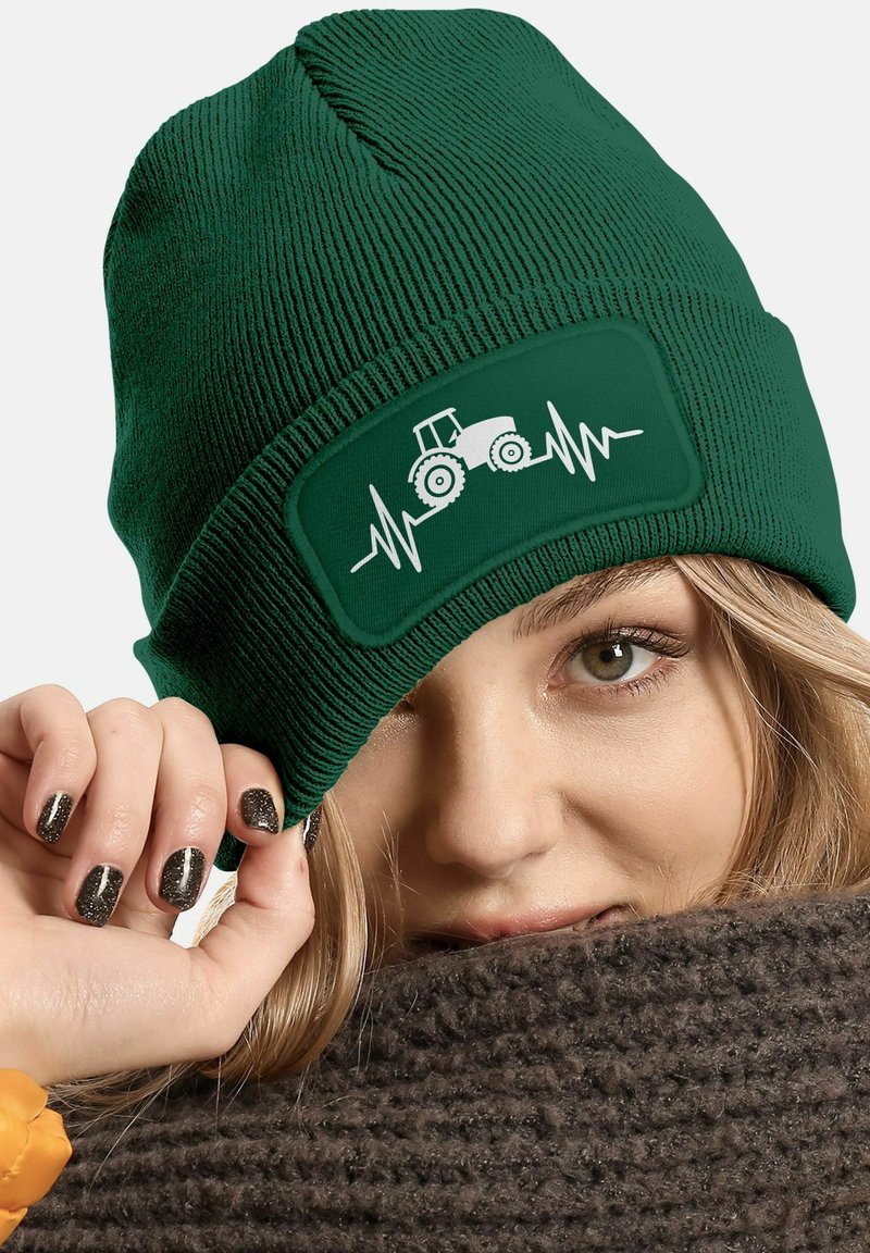 Green knitted beanie featuring a white tractor graphic and heartbeat design on a textured patch. The material is ribbed, creating a snug fit.