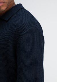 Dunkelblaues, geripptes Baumwoll-Polohemd mit Kragen und strukturiertem Stoff, das ein tailliertes Design und kurze Ärmel zeigt.