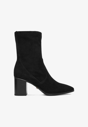 Stivale nero in camoscio fino a metà polpaccio con punta appuntita e tacco spesso a blocco su sfondo bianco uniforme.