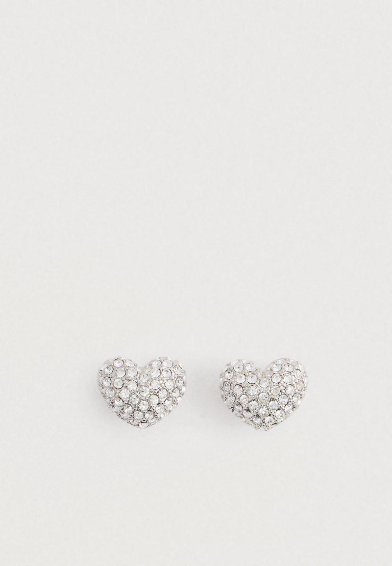Un par de pendientes en forma de corazón de plata engastados con pequeños cristales transparentes sobre un fondo blanco liso.