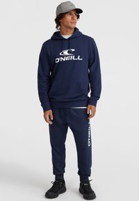 Navy hoodie with white logo, kangaroo pocket, and adjustable drawstring; paired with matching joggers featuring a printed logo down the leg.