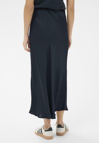 Garšīga, plūstoša tumši zila svārku ar gludu tekstūru un maigu A formas piegriezumu, kombinēta ar gaišas krāsas sporta apaviem ar melniem akcentiem.