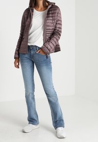 Kurtka pikowana z kapturem w kolorze mauve, w połączeniu z jasnoniebieskimi dżinsami bootcut. Pod spodem znajduje się biała koszulka, a całość uzupełniają białe trampki.