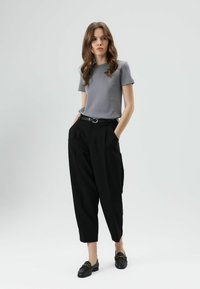 T-shirt gris à manches courtes associé à un pantalon noir taille haute avec ceinture, et des mocassins noirs avec des accents dorés. Textures lisses dans l'ensemble.
