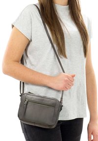 Gray leather crossbody bag with a zippered front pocket, rectangular shape, adjustable strap, and smooth texture. Worn on the shoulder.