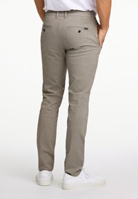 Beige textuur broek met een slim fit, twee achterzakken en subtiele stikdetails. Draagt een paar witte sneakers.