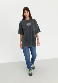 Charcoal oversized t-shirt with "San Diego California" graphic, paired with blue jeans and dark sneakers featuring neon green laces.