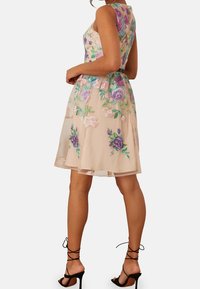 Šaty s květinovou výšivkou, vyrobené z průsvitné, světle broskvové látky s fialovými a růžovými květy. Upnutý korzet, rozšířená sukně a štíhlé ramínka.