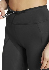 Leggings neri a vita alta con una superficie liscia, dotati di un cordoncino in vita e cuciture laterali per un tocco di design in più.