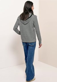 Gestreifter schwarz-weißer Hoodie mit Kordelzug, kombiniert mit blauen, ausgestellten Jeans. Der Stoff wirkt weich; entspannte Passform mit langen Ärmeln.