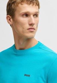 Turquoise t-shirt made of cotton, featuring a crew neck, short sleeves, and a small black "BOSS" logo on the chest. Smooth texture.