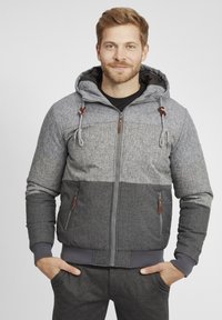 Grey hooded jacket with mixed textures; lighter grey top and darker grey bottom, featuring zippered pockets and adjustable drawstrings.