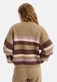 Strikkegenser i brunt med horisontale striper i krem, mauve og burgunder. Myk tekstur, oversized passform, og ribbestrikkede mansjetter og søm.