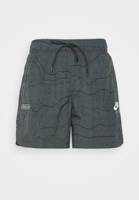 Black swim shorts with a grid pattern and dark wavy lines. Features a drawstring waistband and Nike branding in white on the side.