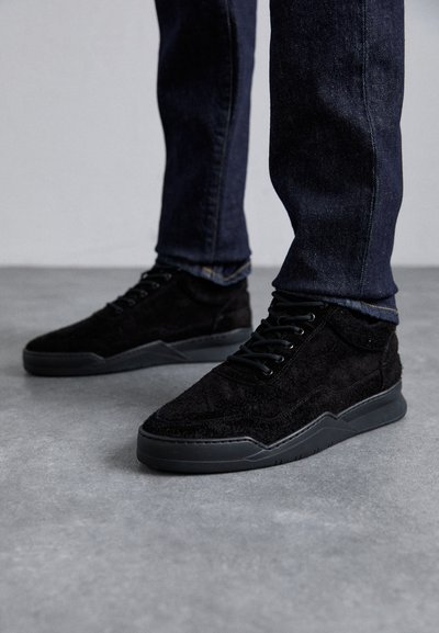 Svarta mockaskor med texturerad yta och gummisulor. Funktioner inkluderar svarta snörningar och en låg profil. Jeans synliga ovanför.
