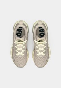 Αθλητικά παπούτσια σε ανοιχτό μπεζ με επάνω μέρος από δίχτυ, κρέμ κορδόνια και διακριτικές κίτρινες λεπτομέρειες. Ορατά τα κείμενα "RUN" και "ROAD" στις εσωτερικές σόλες.