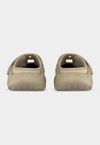 Ζευγάρι μπεζ παπούτσια τύπου slip-on με μαλακές σόλες και λεπτομέρειες από ύφασμα δίχτυ, εμφανιζόμενα από πίσω σε λευκό φόντο.